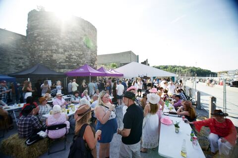 Guests at tables on the quay below the town walls, with gazebos and stalls behind.