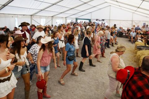 Rows of line dancers in cowboy hats and boots in the marquee.