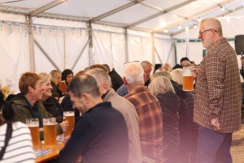 Guests laughing at long tables in the marquee, steins of beer in hand.