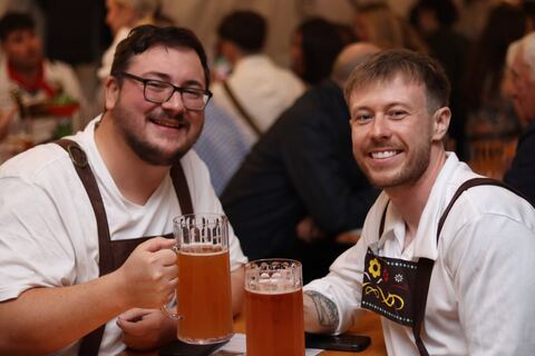 Two friends in lederhosen raise their steins at the table.