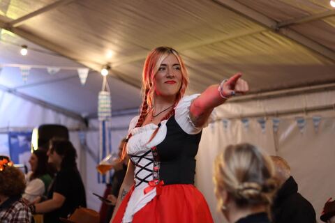 A woman in a red dirndl points across the marquee, singing along.