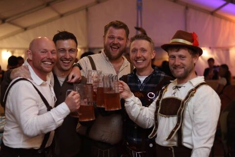 Five friends in lederhosen raise their steins together.