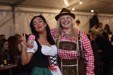 Two friends in a dirndl and lederhosen pose arm in arm.